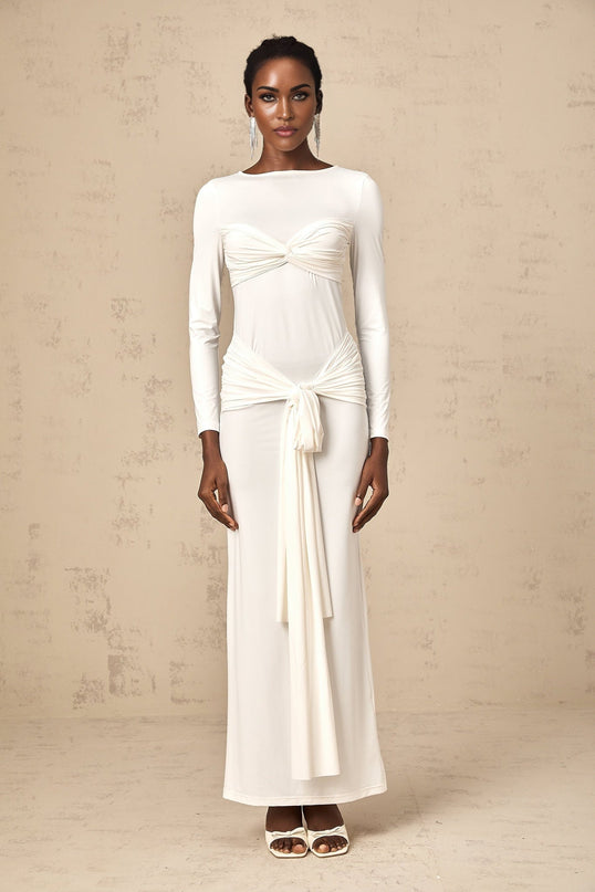 A long white maxi dress with ruched detailing and a twisted ribbon accent worn by a model