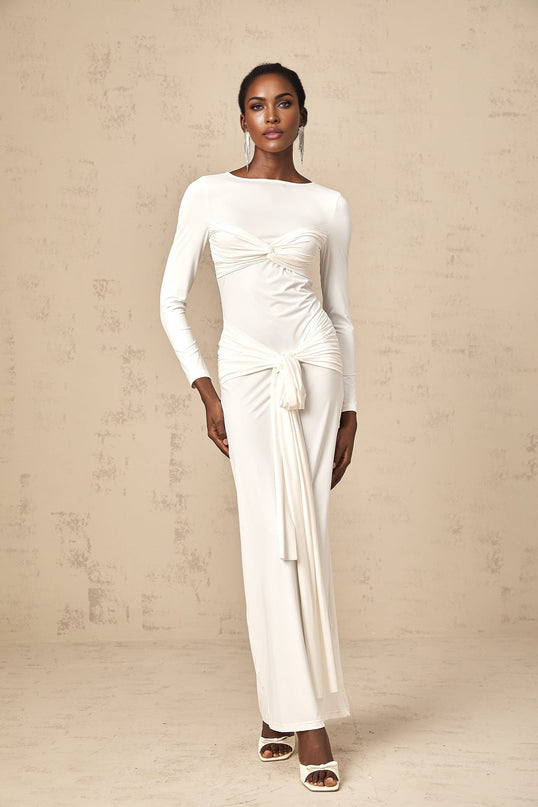 A long white maxi dress with ruched fabric featuring a twist detail and ribbon accents