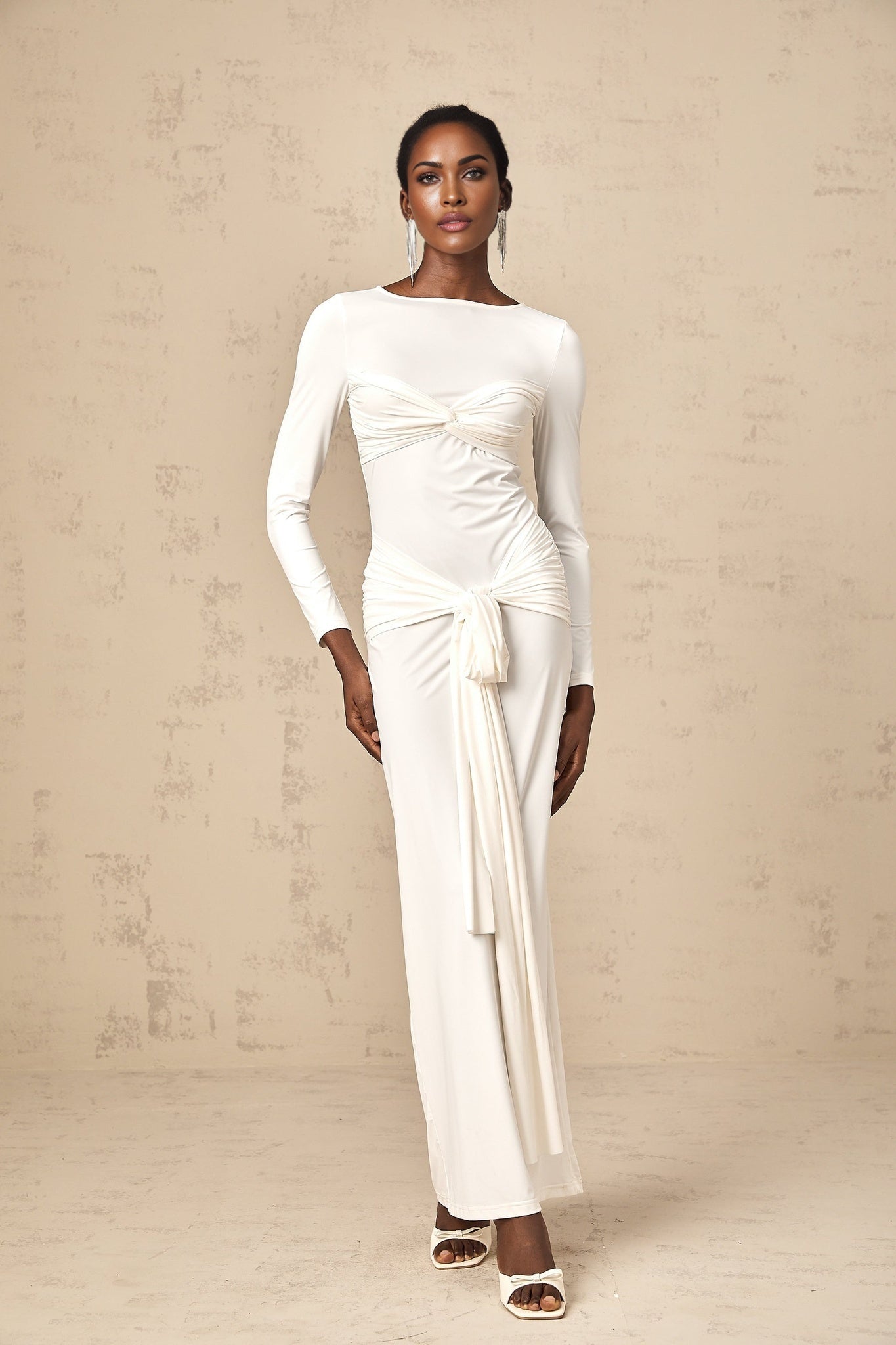 A long white maxi dress with ruched fabric featuring a twist detail and ribbon accents