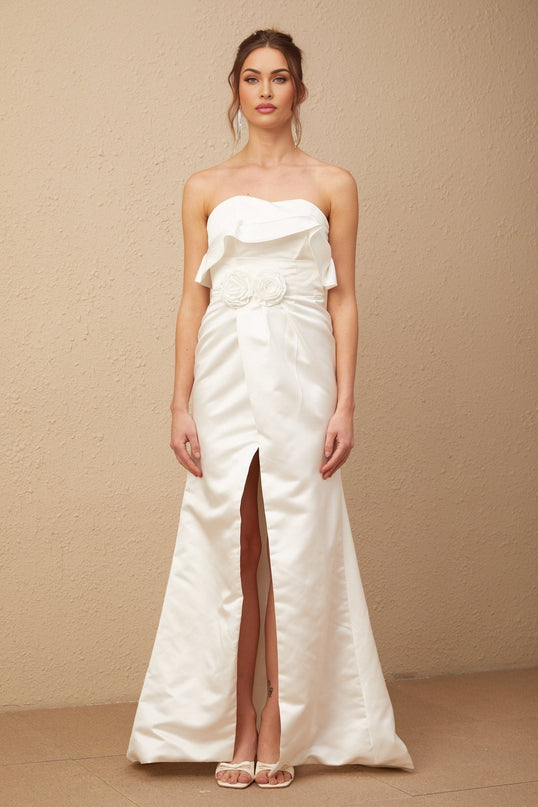 A long white satin dress with floral appliques adorning the bodice and skirt featuring a flowing maxi length silhouette