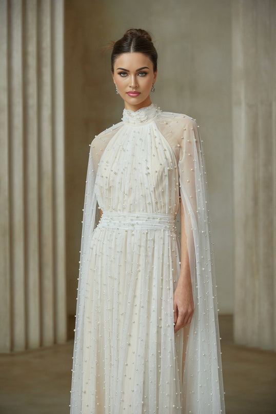 A long white tulle maxi dress with a cape design and embellishments featuring a flowy silhouette and elegant details