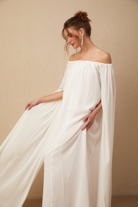 A long white tulle maxi dress with a capelike design and draped elements featuring a flowy silhouette and ethereal appearance