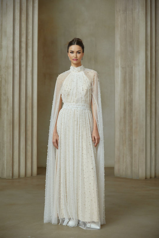 A long white tulle maxi dress with cape design and embellishments featuring a flowy silhouette and delicate detailing