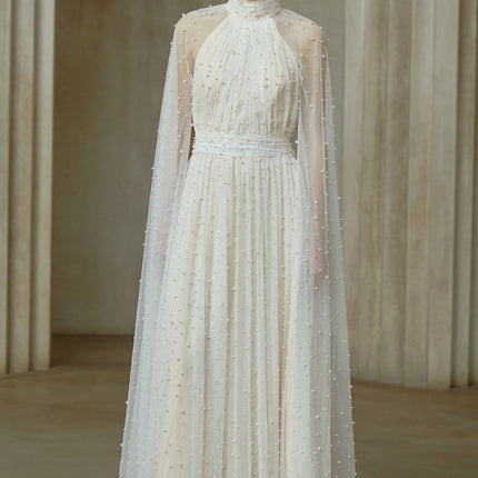 A long white tulle maxi dress with cape design and embellishments worn by a model against a plain background