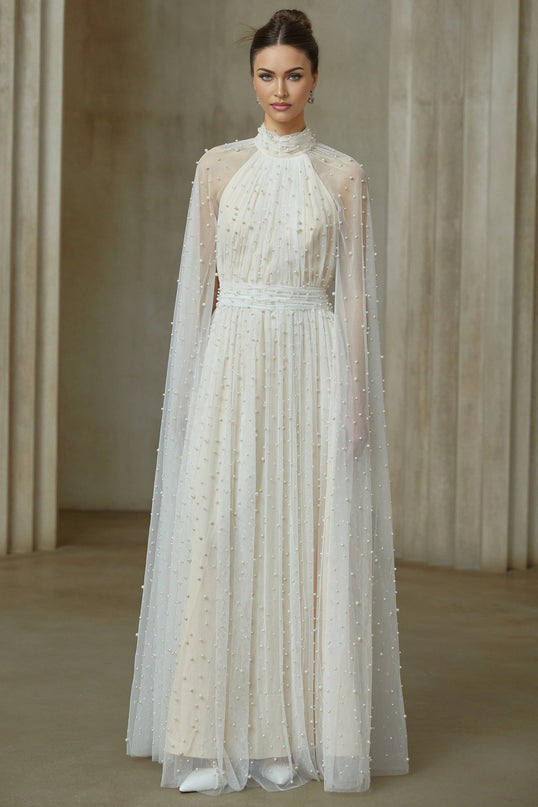 A long white tulle maxi dress with cape design and embellishments worn by a model against a plain background