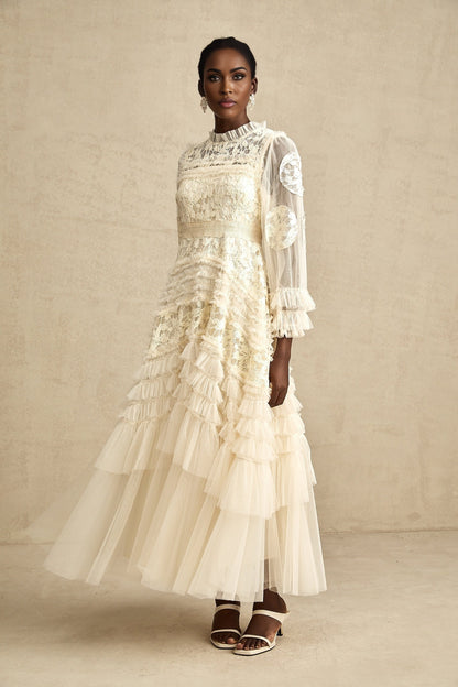 A long white tulle maxi dress with layers of sheer fabric featuring delicate floral embroidery in pastel colors