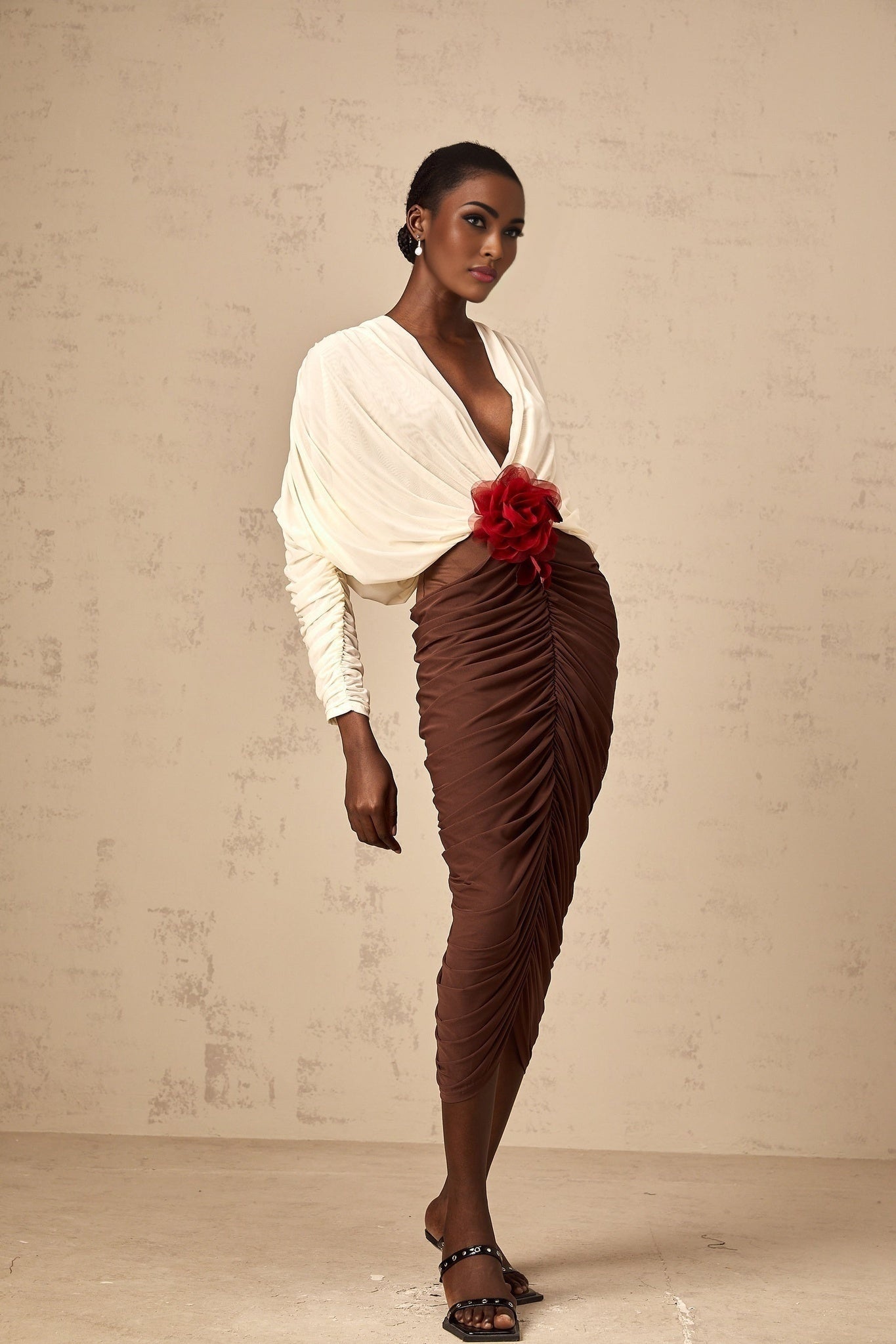 A midi dress with ruched detailing featuring color blocking and a decorative flower brooch The dress is named Leontine and has a stylish contemporary design