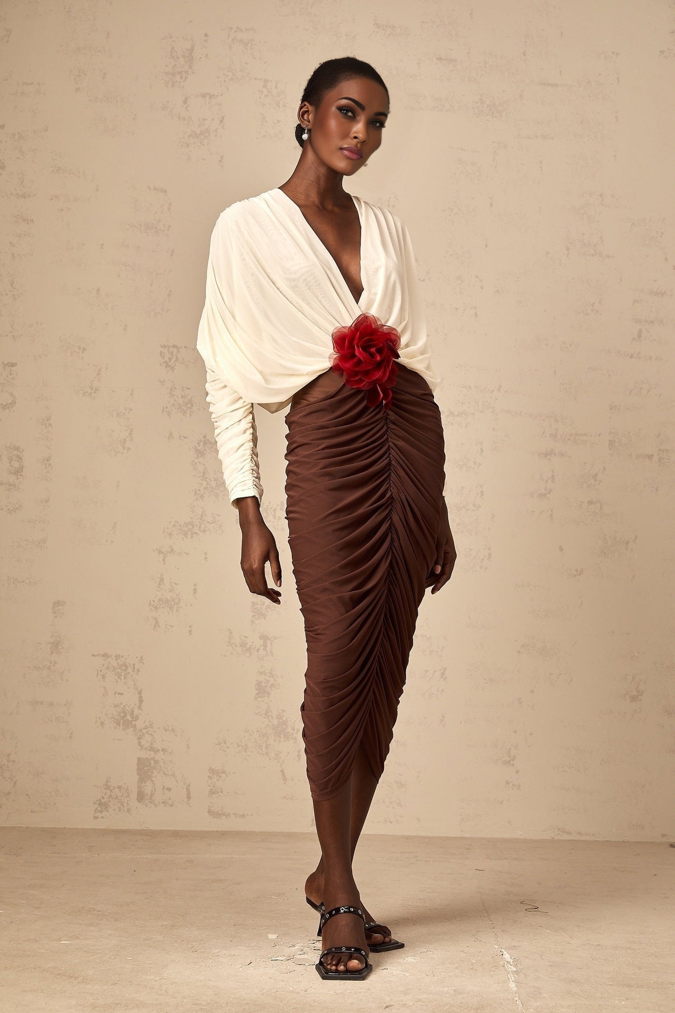 A midi dress with ruched detailing featuring colorblocked sections and a decorative flower brooch The dress is named Leontine and has a feminine silhouette