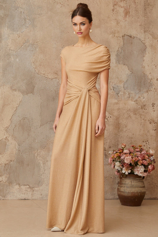A model wearing a long gold maxi dress with an asymmetrical hemline and pleated details The dress features a sleeveless design and a flowing silhouette