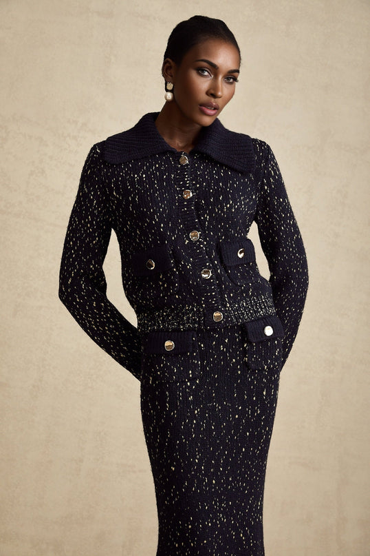 A navy blue crochet knit jacket and matching skirt set worn by a model standing against a plain background