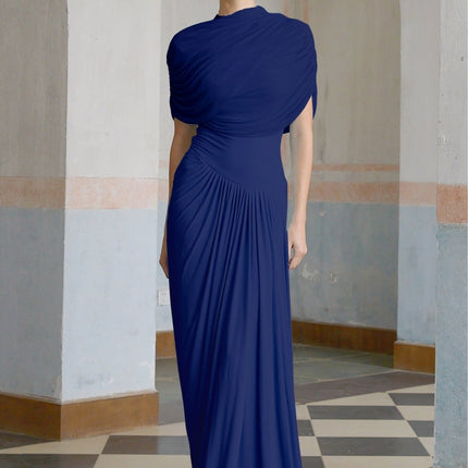 A navy blue long maxi dress with an asymmetric design and pleated details worn by a model standing against a plain background