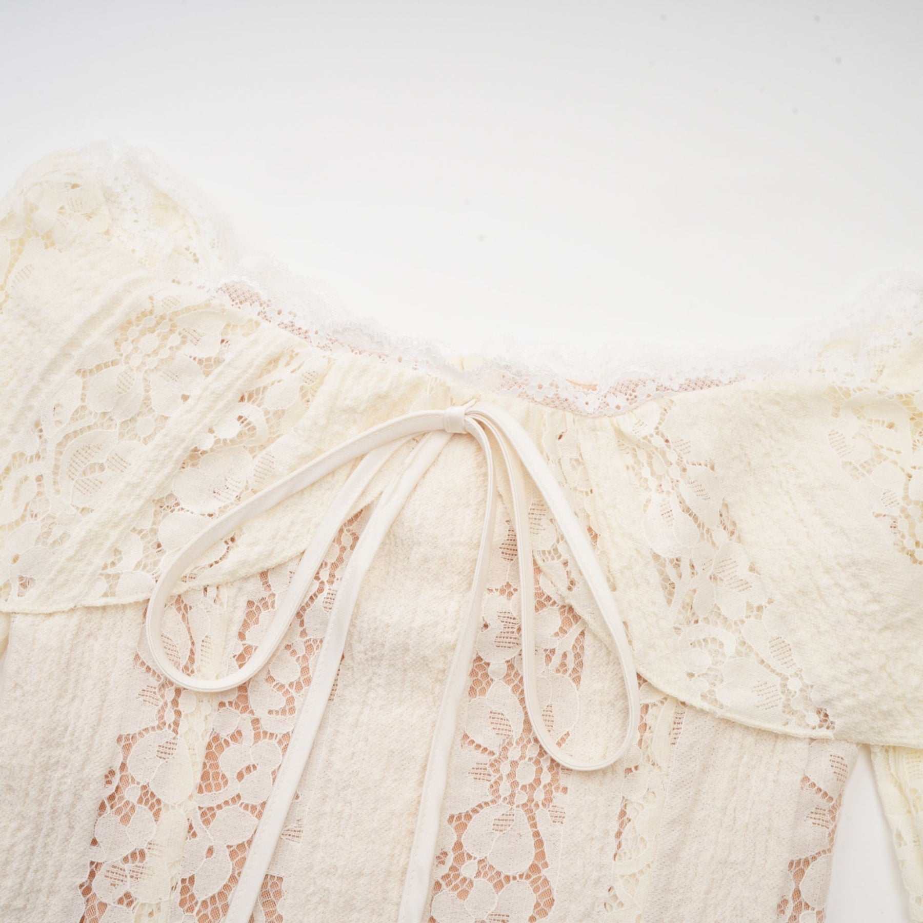 A neutral colored mini dress with floral lace pattern and flared cuffs named Émeline