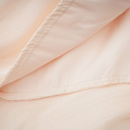 A neutral colored mini dress with full pleats and ruffles featuring a feminine Eugenie style design