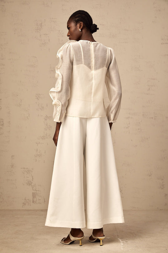 A neutralcolored blouse with delicate threedimensional flower details on sheer fabric creating a soft and feminine appearance