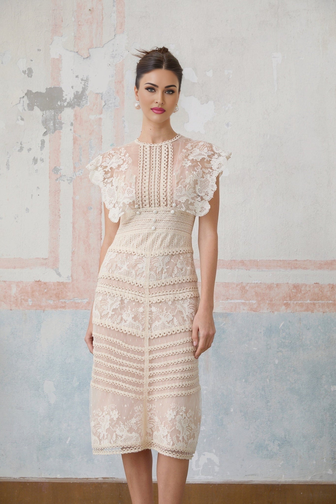 A neutralcolored midi dress with floral embroidery and lace details on a model against a plain background