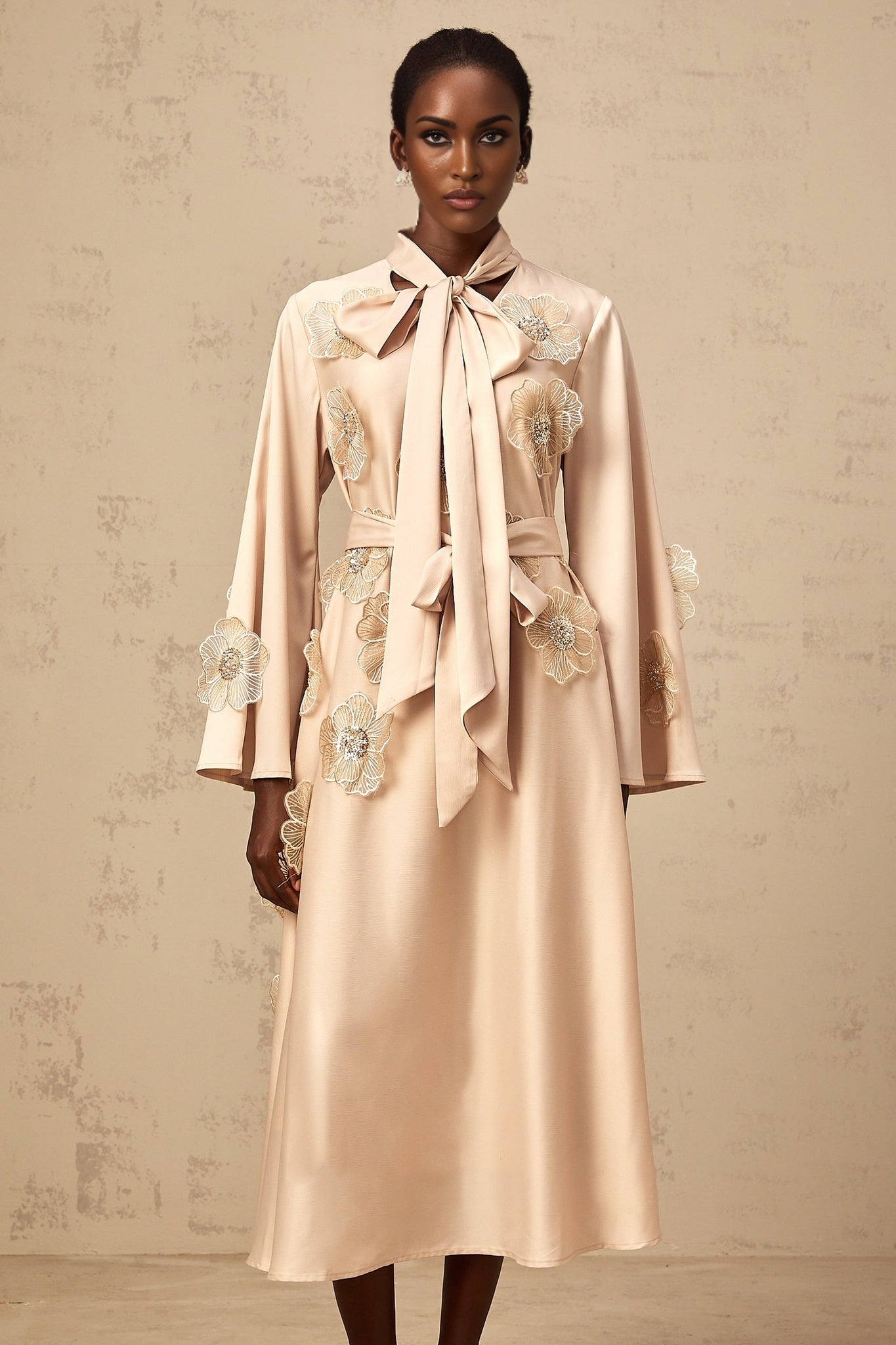 A neutraltoned flared midi dress with a tie detail and floral applique decorations featuring an Orane design