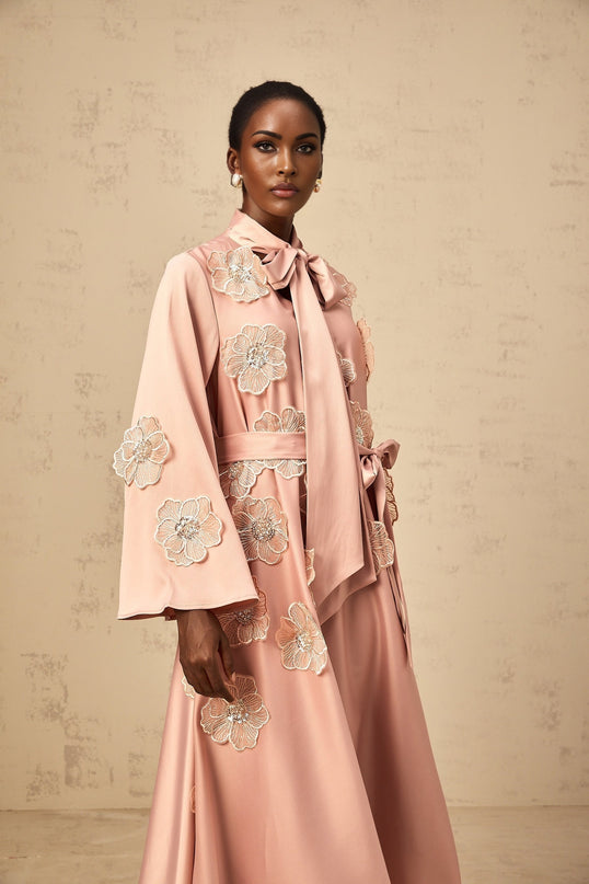 A pink flared midi dress with a tied waist and floral applique details