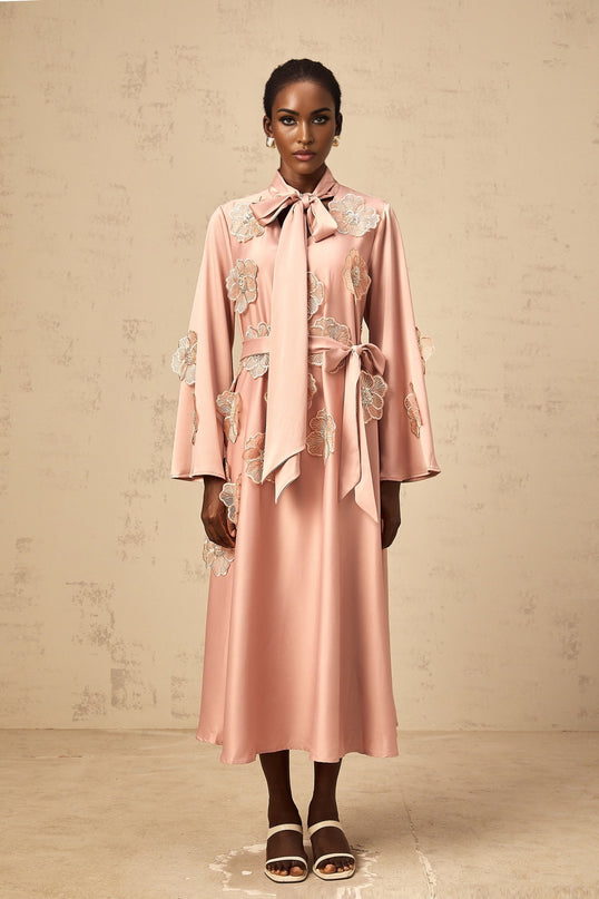 A pink flared midi dress with floral applique details and a tied waist featuring a vibrant orange pattern