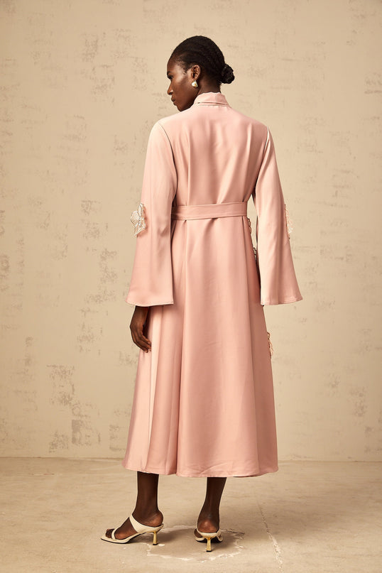 A pink flared midi dress with tied waist and floral applique details