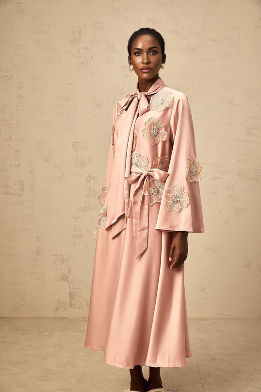 A pink flared midi dress with tied waist and floral applique details