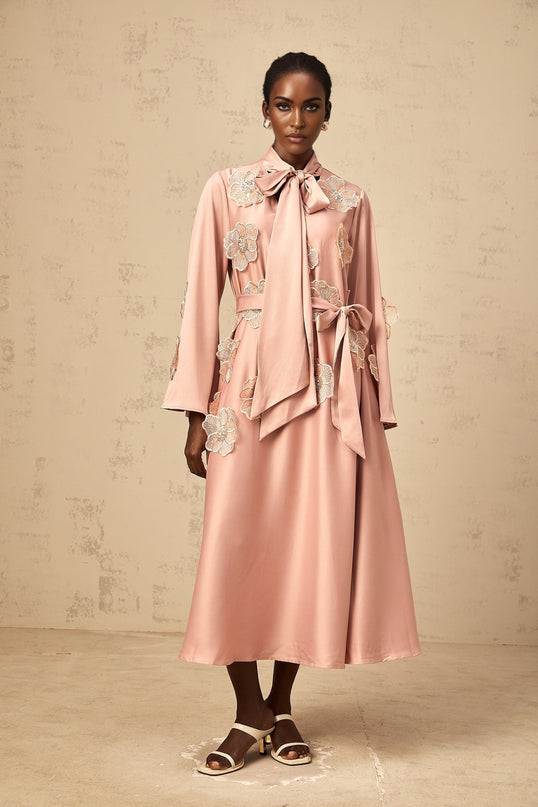 A pink flared midi dress with tied waist and floral applique details