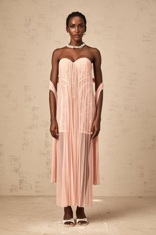 A pink floorlength dress with a pleated tulle skirt and ribbon design details worn by a model against a plain background