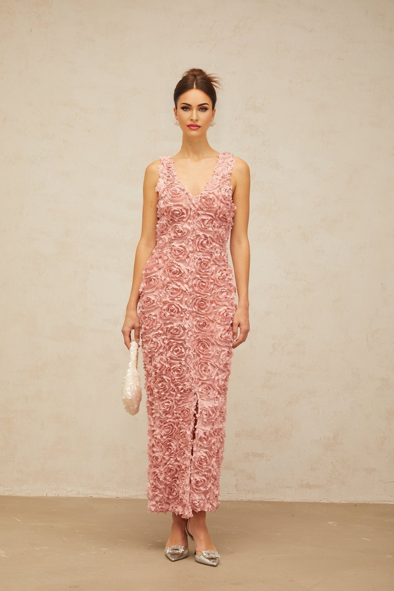 A pink floral maxi dress with a Vneck and faux flower details worn by a model standing against a plain background