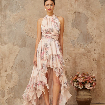 A pink maxi dress with an asymmetrical hemline and floral print pattern worn by a model standing against a plain background