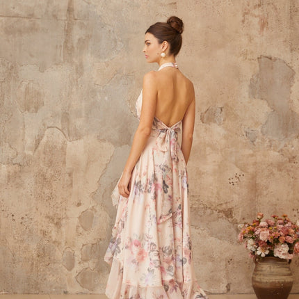 A pink maxi dress with an asymmetrical hemline featuring a floral print pattern worn by a model against a plain background