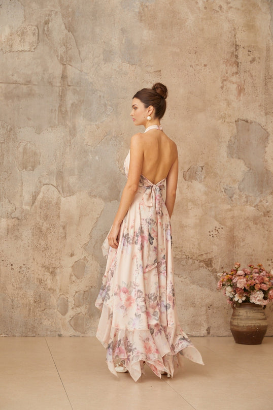 A pink maxi dress with an asymmetrical hemline featuring a floral print pattern worn by a model against a plain background