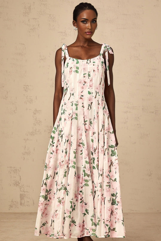 A pink maxi dress with floral print and tied straps worn by a model against a plain background