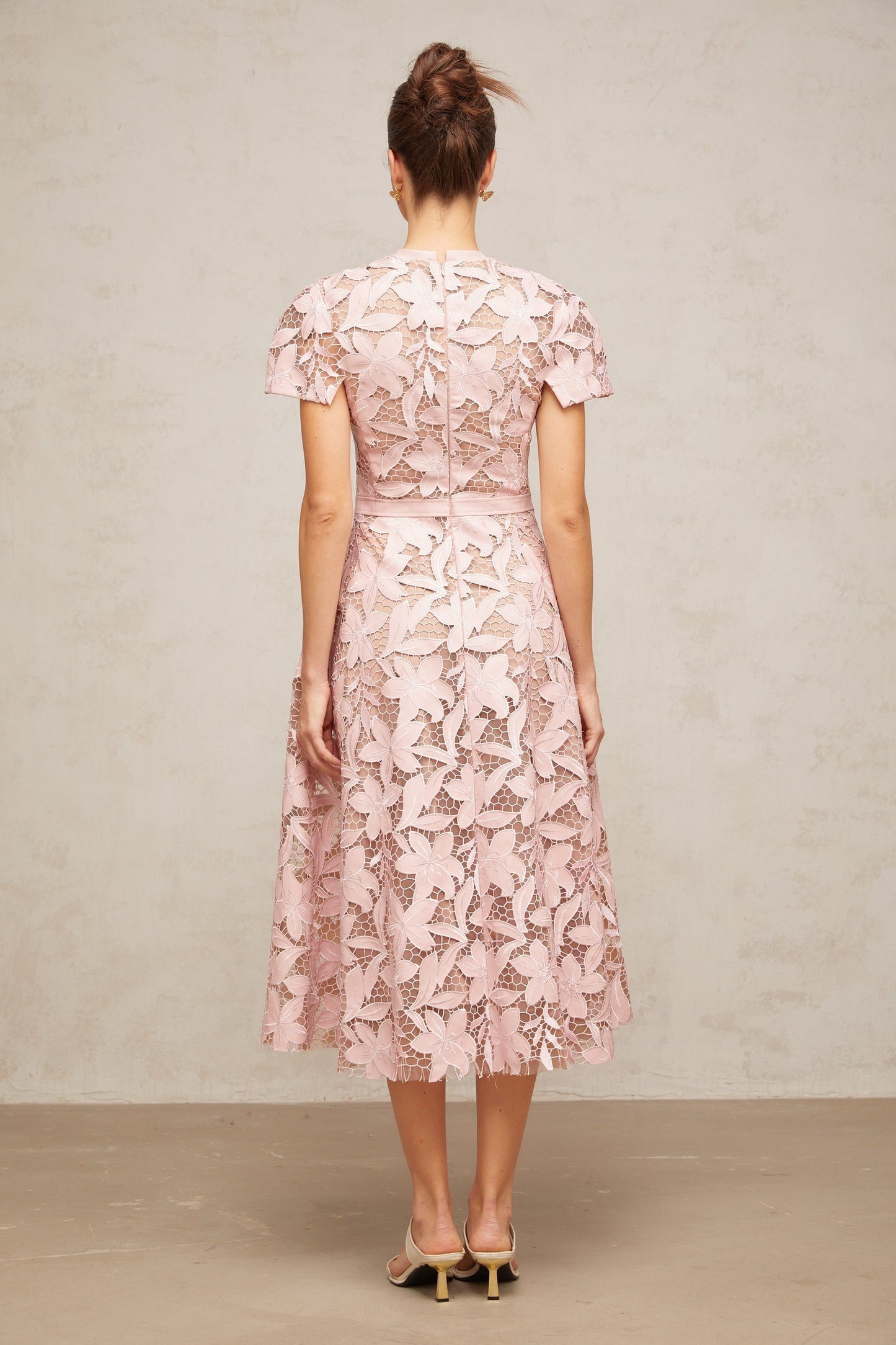 A pink midi dress made of delicate guipure lace featuring intricate floral patterns and a feminine silhouette