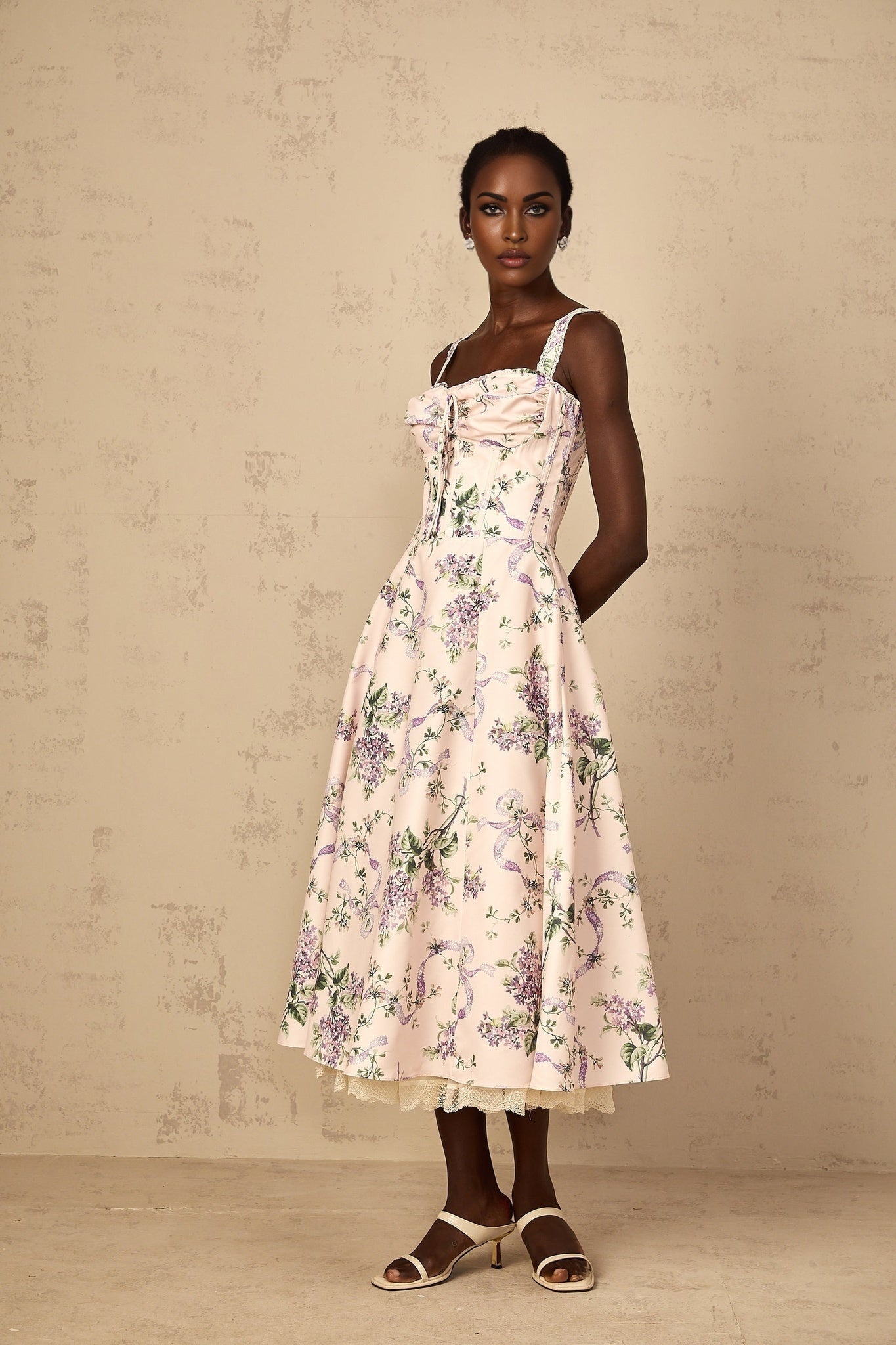 A pink midi dress with a floral print pattern featuring shirred detailing worn by a woman
