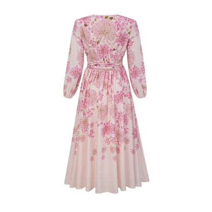 A pink midi dress with a floral print pattern worn by a model standing against a plain background