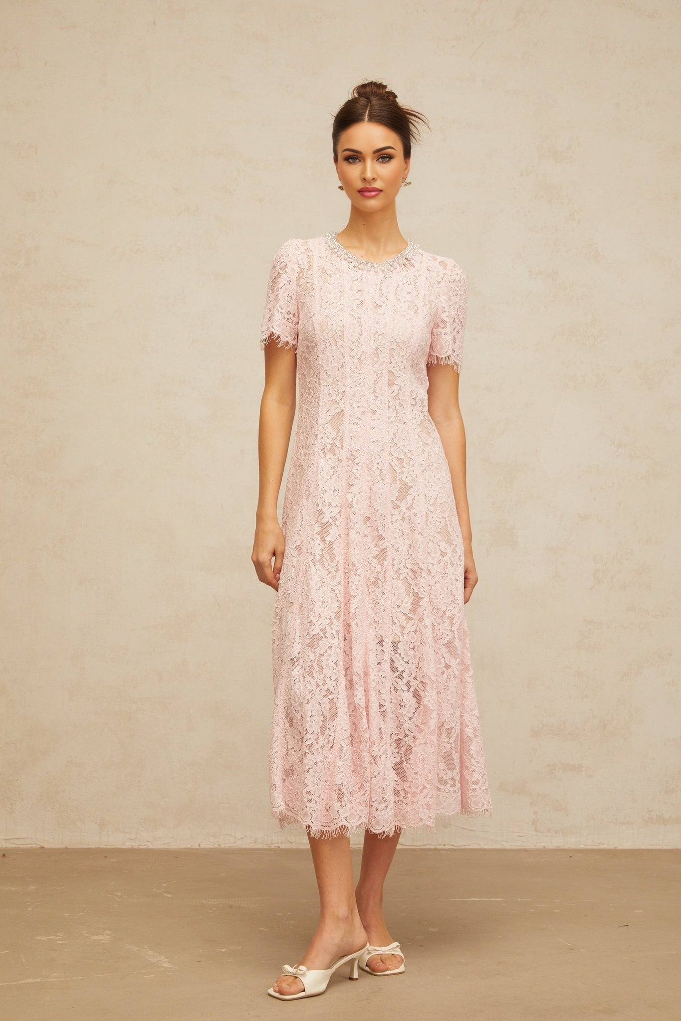 A pink midi dress with floral lace pattern and embellishments on a mannequin or model against a plain background