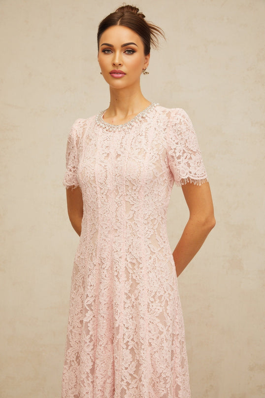 A pink midi dress with floral lace pattern and embellishments on a plain background