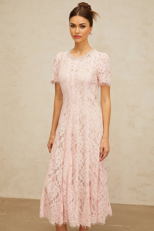 A pink midi dress with floral lace pattern and embellishments worn by a model against a plain background