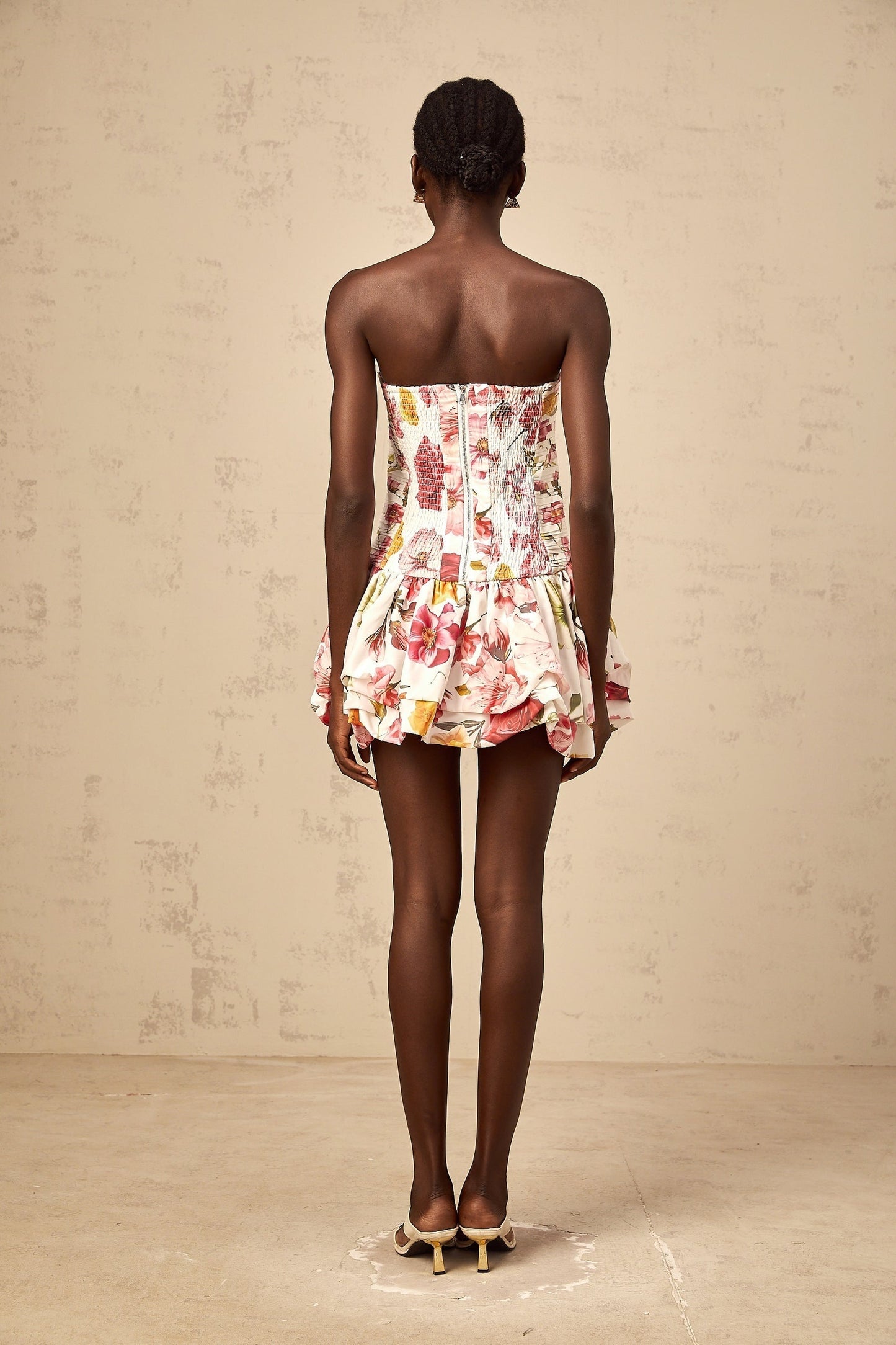 A pink mini dress with a floral print pattern and smocked details featuring a design by Ines