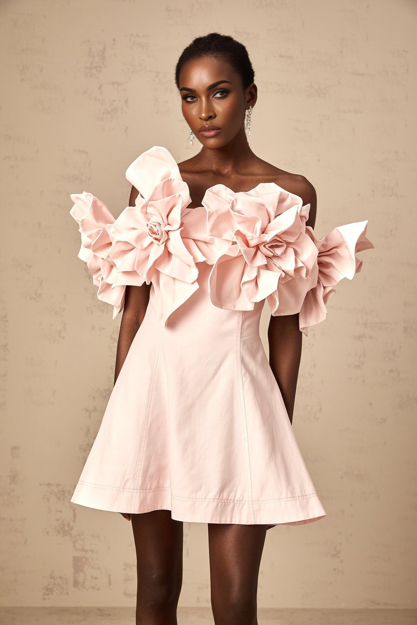 A pink mini dress with an offshoulder neckline featuring three dimensional petal embellishments and a short hemline