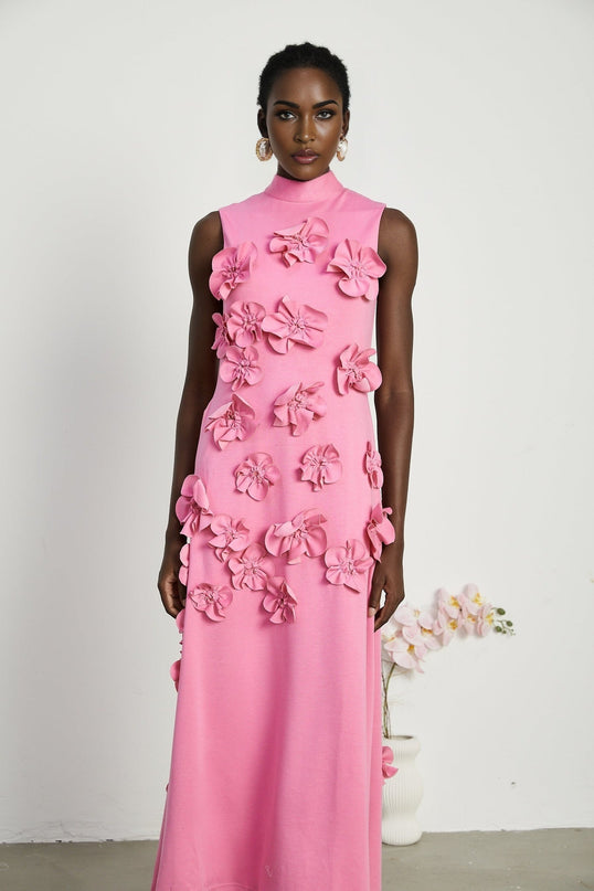 A pink sleeveless maxi dress with a bow and decorative artificial flowers