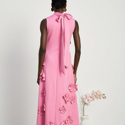 A pink sleeveless maxi dress with a bow and decorative artificial flowers