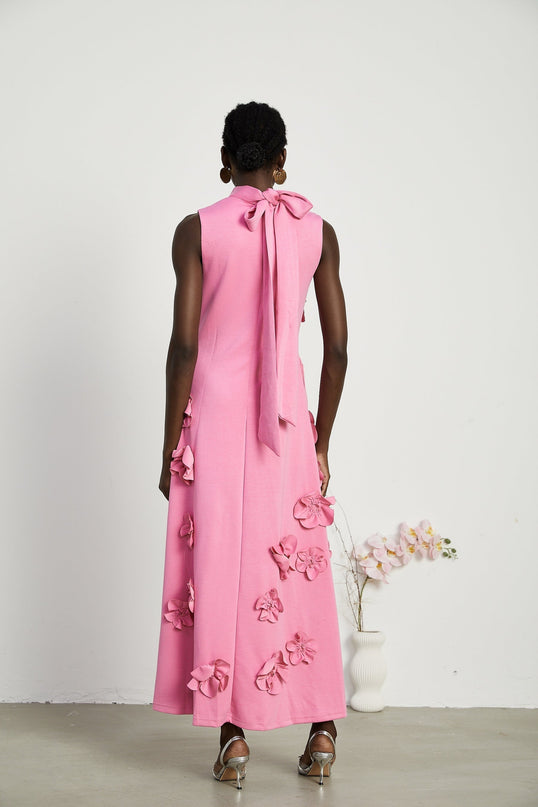 A pink sleeveless maxi dress with a bow and decorative artificial flowers