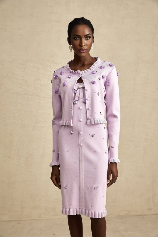 A purple knitted cardigan and dress set with faux flower embellishments on a white background The dress features a floral pattern while the cardigan has a solid color Both pieces are made of soft knit fabric creating a matching ensemble