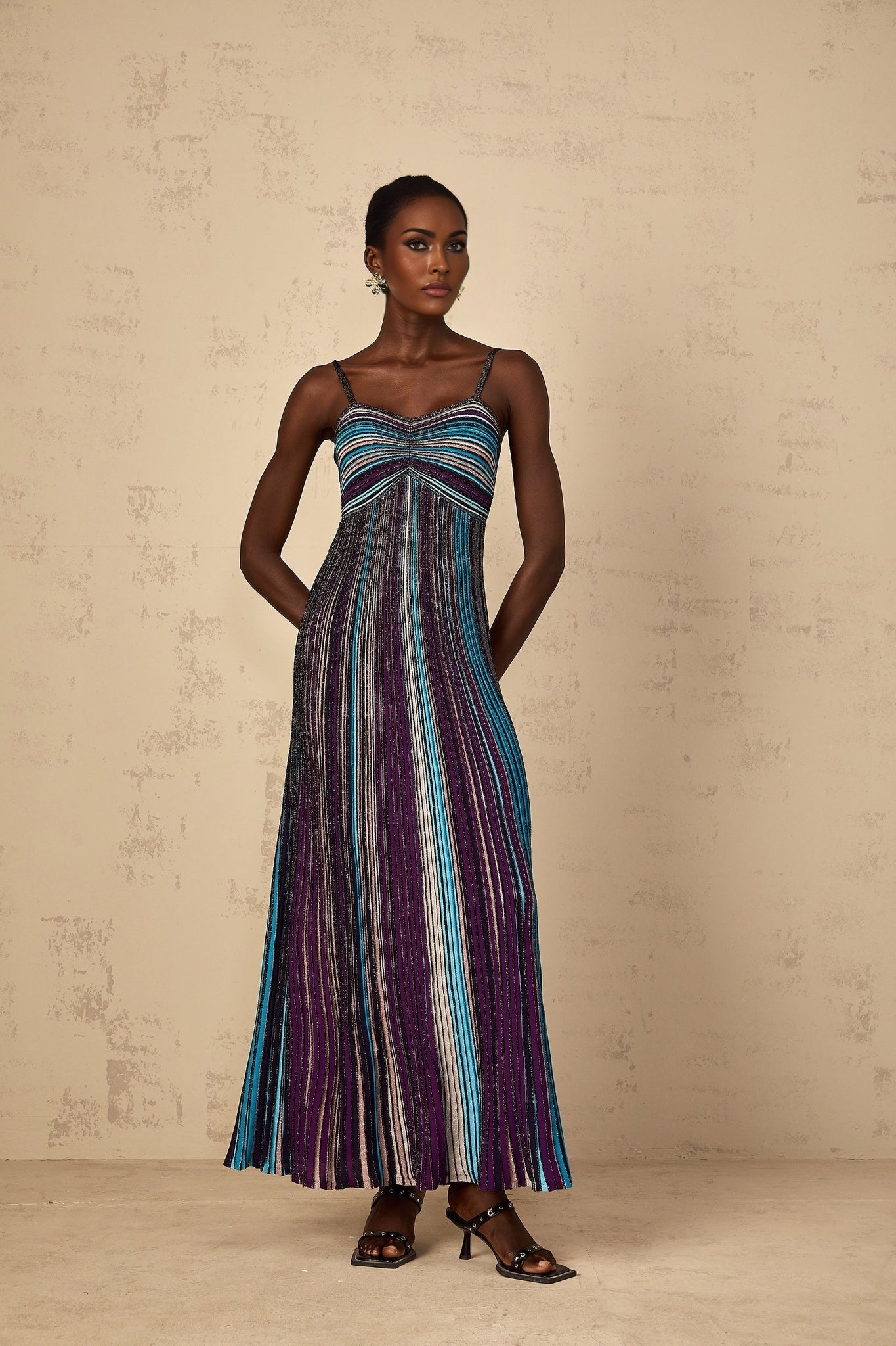A purple maxi dress with sequin striped pattern and knit fabric worn by a woman standing against a plain background