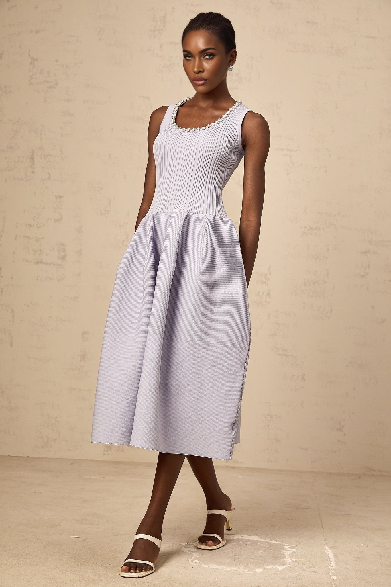 A purple midi dress with ribbed knit fabric and embellishments worn by a model against a plain background