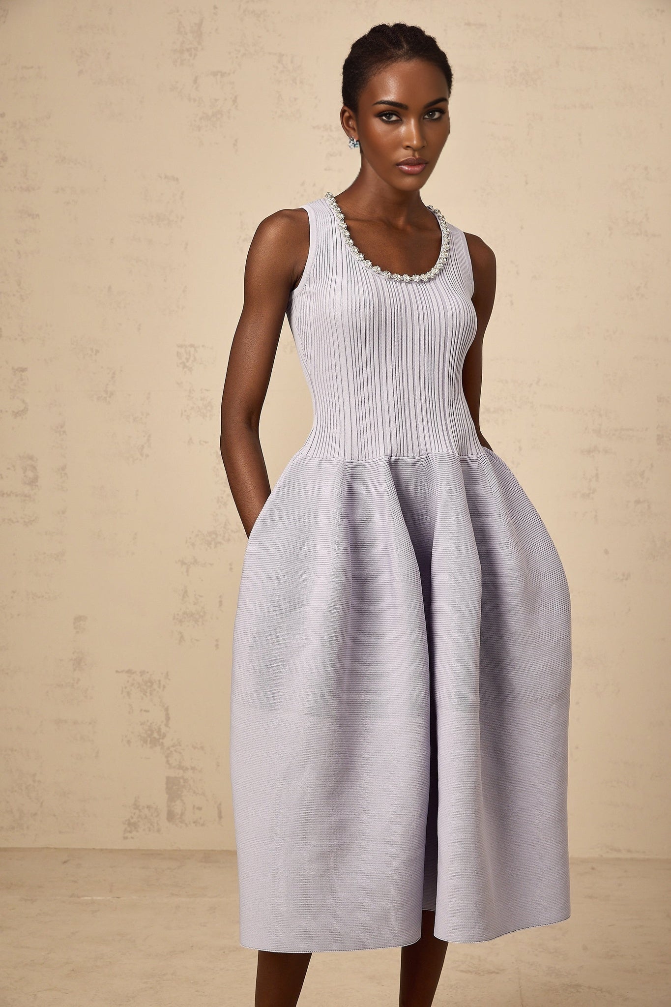 A purple ribbed knit midi dress with embellishments worn by a model standing against a plain background