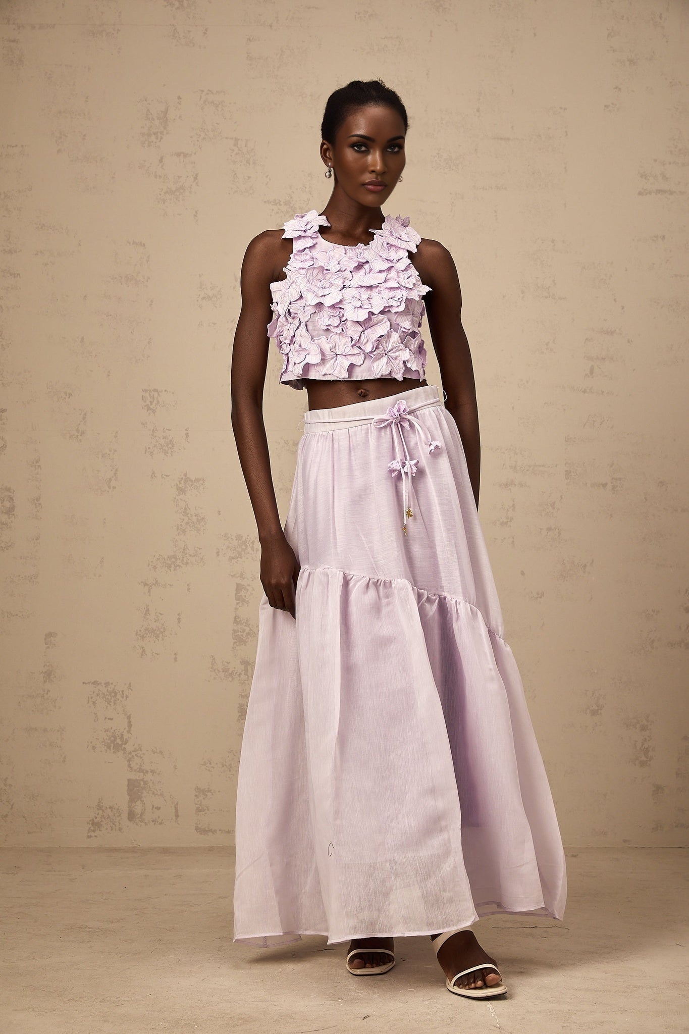 A purple twopiece outfit consisting of a sleeveless top and matching skirt adorned with faux flowers creating a floral pattern throughout the set