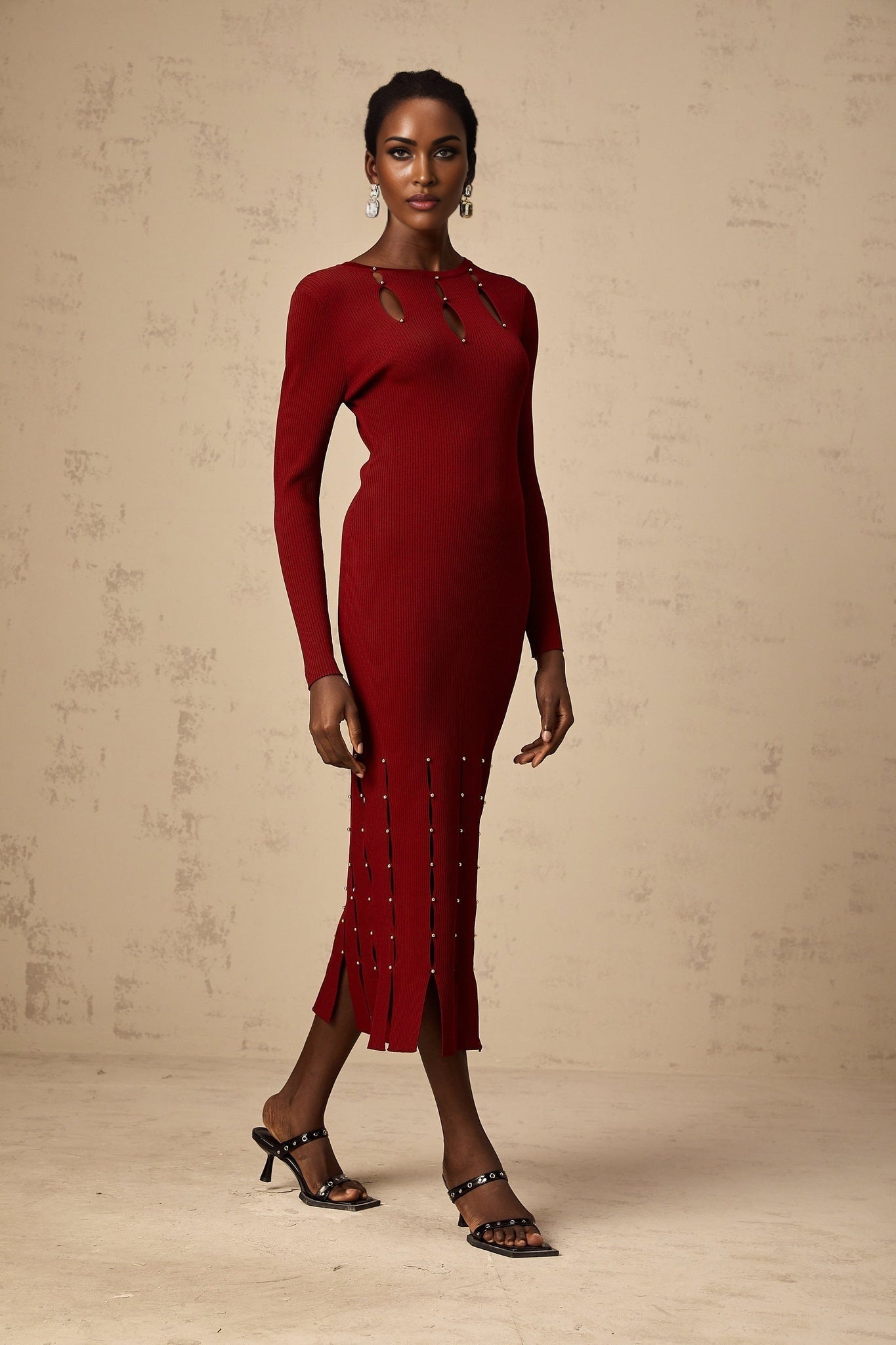 A red knit midi dress with long sleeves beaded detailing and cutout design worn by a model
