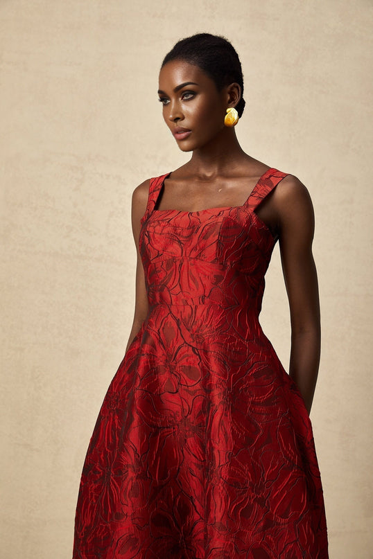 A red midi dress with a floral jacquard pattern worn by a model standing against a plain background