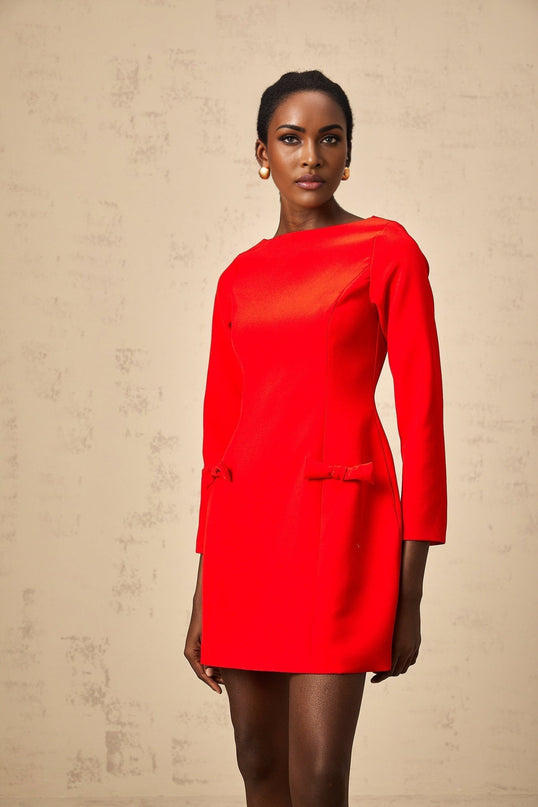 A red mini dress with long sleeves and a bowknot detail worn by a model against a plain background